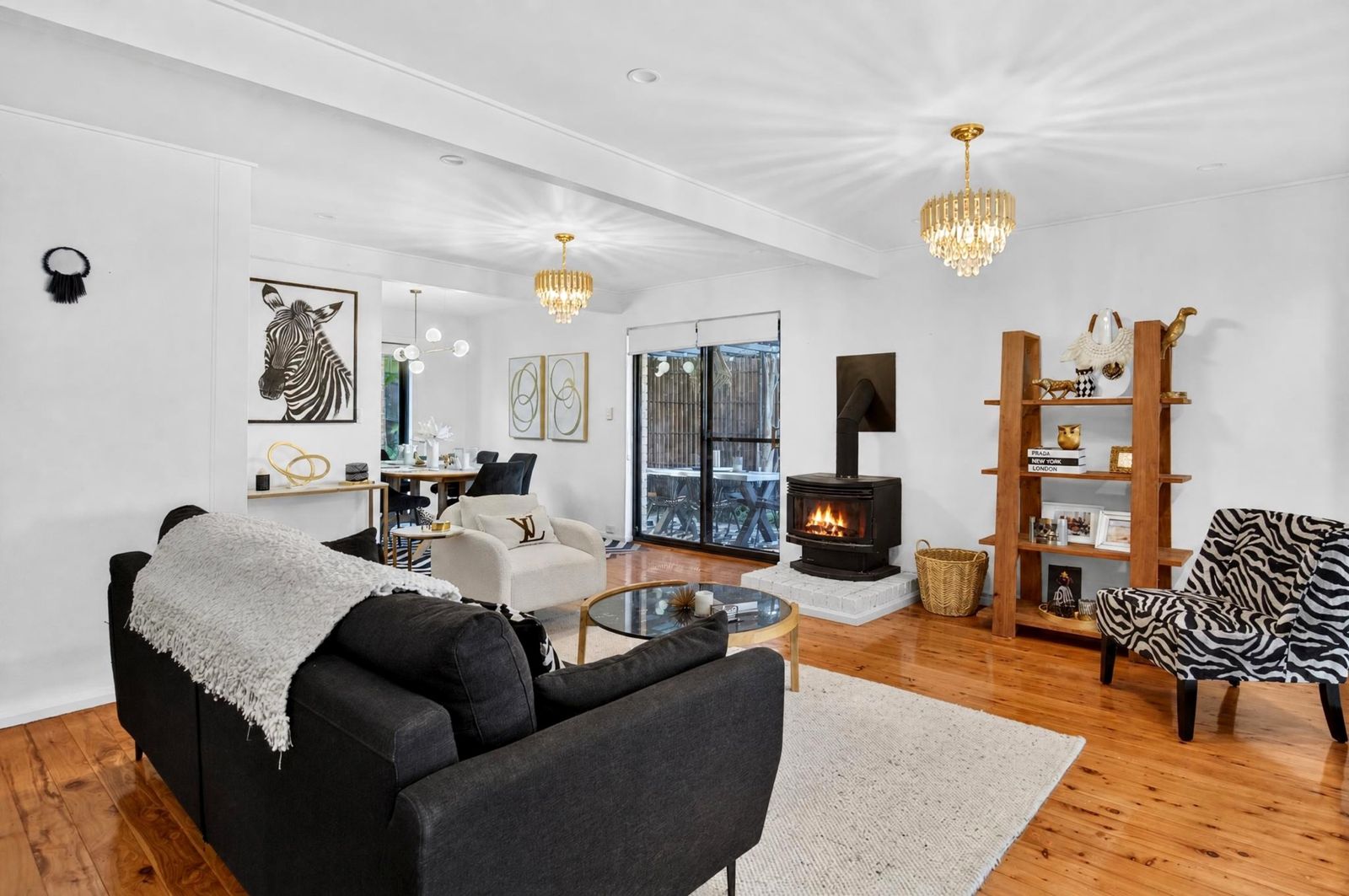 Living room with a charcoal sofa, cream armchair, wood fireplace, gold chandeliers and timber floors